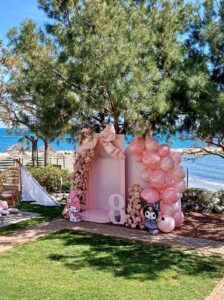 Pastel pink kids’ birthday party setup in the sea view garden of Crowne Plaza Limassol, featuring outdoor seating, balloons and coastal scenery. sea view kids’ birthday party